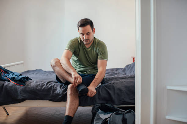 istock Workout Preparations at Home: a Determined Fit Handsome Man Sitting on Bed and Putting on Socks and Sneakers to go Running 1226096048