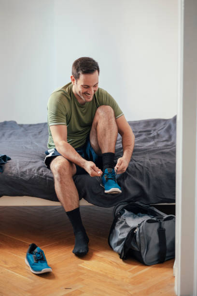 istock Workout Preparations at Home: a Happy Fit Handsome Man Sitting on Bed and Putting on Socks and Sneakers to go Running 1226096051
