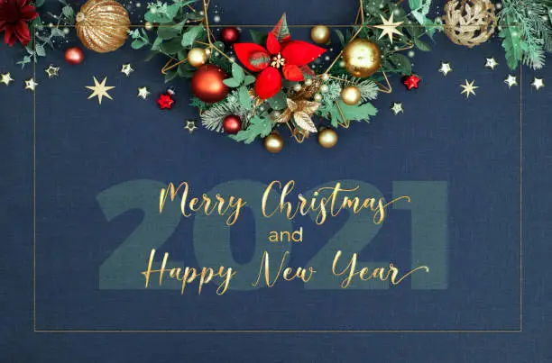 Merry Christmas and Happy New Year 2021!. Decorative Christmas border, floral garland with eucalyptus, baubles, trinkets and red poinsettia. Red, green, golden Xmas decorations on classic blue linen background.