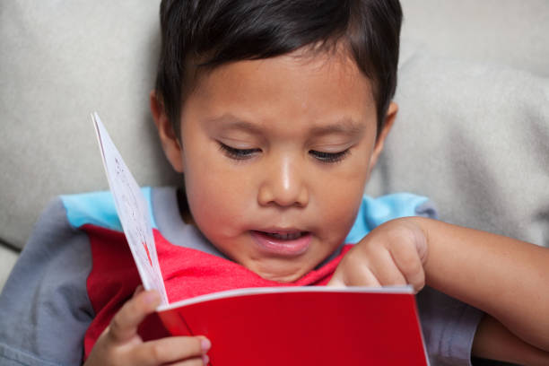 A preschooler pronouncing  simple phonics is reading from an early reader style story book. stock photo