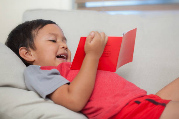 A young reader holding a simple book in his hand and reading out loud while relaxed on a couch. stock photo
