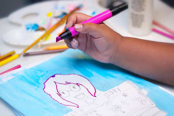 A little kids hand holding a pink art marker and coloring inside the lines of a hand drawn illustration using mixed media. stock photo