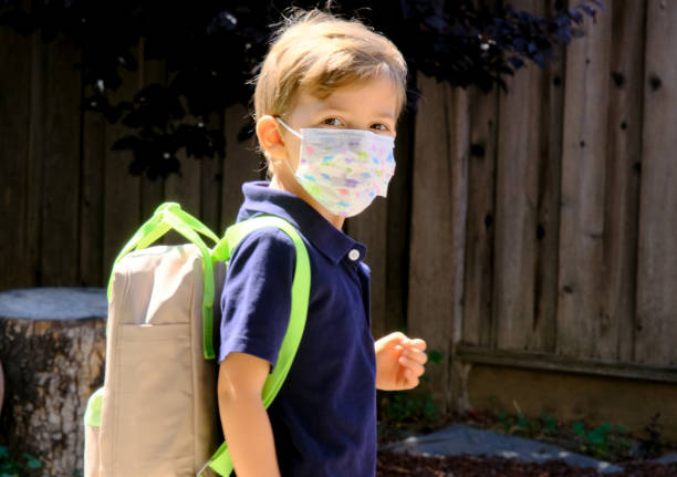 little schoolboy wearing a protective mask and a backpack - little boys preschooler back to school backpack imagens e fotografias de stock