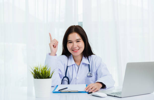 istock Asian doctor young beautiful woman smiling using working with laptop computer and her writing something on clipboard white paper and point finger up at hospital desk office, Healthcare medical concept 1226103058
