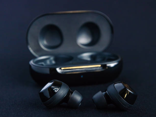 istock Earbud headphones side profile - displayed in front of opened black wireless earbud charging case on black background. 1226105683