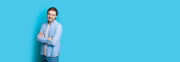 istock Caucasian man with long hair and beard posing while crossing hands on a blue wall with free space 1226107339
