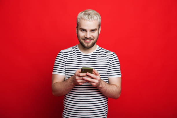 istock Blonde caucasian man chatting with his friends on a red background while looking at camera 1226113798