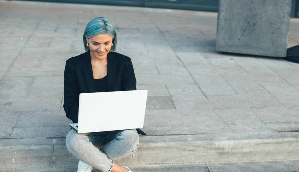 istock Caucasian lady with blue hair posing outside with a computer while sitting and working 1226116635