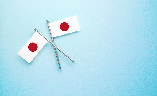 Tiny  Japanese flag pair on light blue background. Horizontal composition with copy space. Directly above.