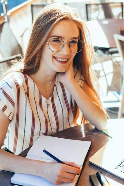 istock Delightful student with red hair and freckles making some notes while wearing eyeglasses and using laptop in a cafeteria 1226121874