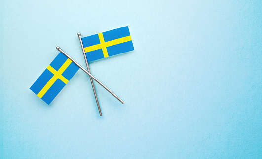 Tiny Swedish flag pair on light blue background. Horizontal composition with copy space. Directly above.