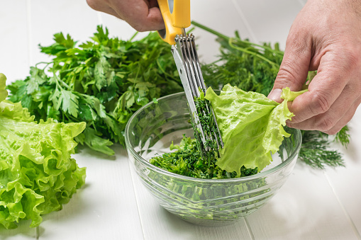 A man cuts fresh herbs into a glass salad bowl. The process of preparing a vegetarian dish.