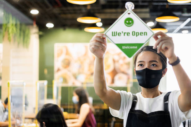 la femme asiatique de propriétaire d’affaires portent le masque protecteur ppe ppe signe ouvert à son restaurant / café, ouvert encore après verrouillage vers le bas en raison de l’éclosion de coronavirus covid-19 - horizontal business open clean photos et images de collection