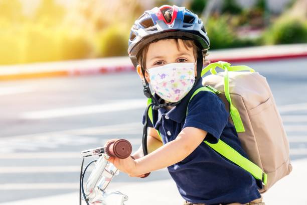 niño pequeño montando una bicicleta usando una máscara protectora y una mochila - little boys preschooler back to school backpack fotografías e imágenes de stock