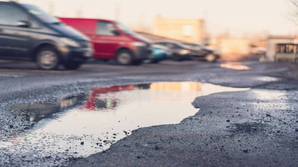 istock puddle in pit on destroyed asphalt road against blurry cars at spring sunset 1226146612