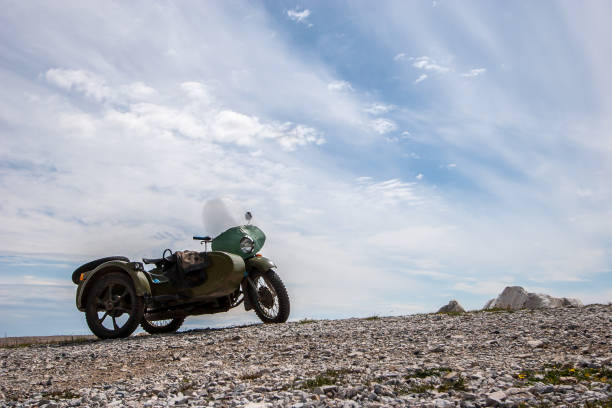 ein altes sowjetisches motorrad mit beiwagen steht mit wolken auf den steinen gegen den himmel. grüne farbe. windschutzscheibe und runder scheinwerfer. horizontale. - sidecar motorcycle past old stock-fotos und bilder