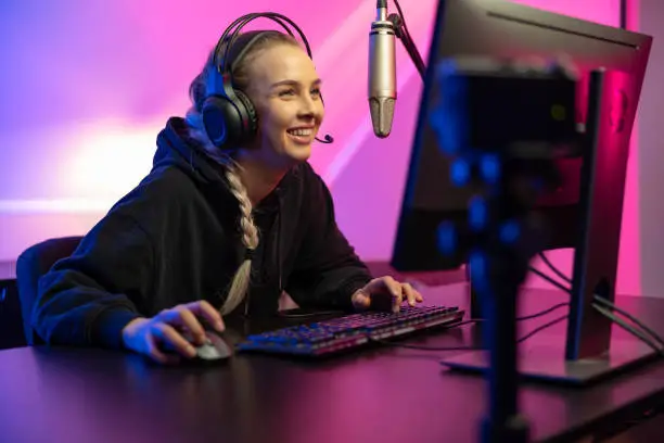 Photo of Professional smiling esport gamer girl live streaming and plays online video game on PC