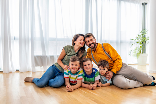 At home, Cheerful family of five persons sitting on wooden floor in the living-room. They are smiling while looking at camera