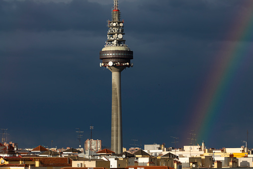 Madrid, Spain - May 19, 2020: Torrespaña digital television and radio tower on a rainy and stormy day with dark clouds in the background and a slight rainbow.
