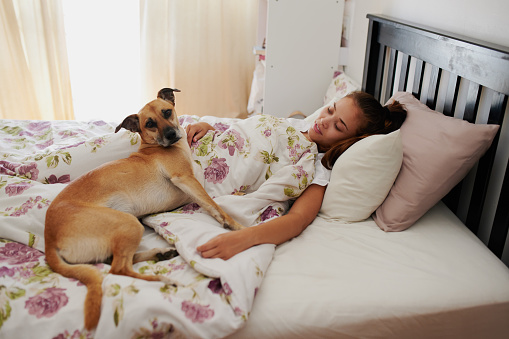 Shot of a young woman relaxing in bed with her dog