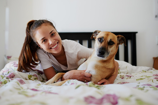 Shot of a young woman relaxing in bed with her dog