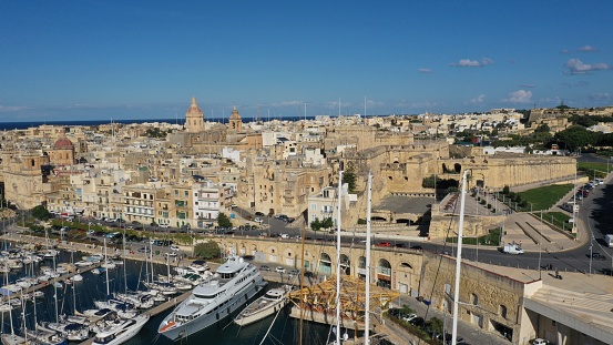 Aerial view of sailboats moored in harbour Senglea and Birgu, Bormla / Cospicua, Valletta, Malta. Ancient architecture of old town: christian orthodox churches, cathedrals, basilicas. Sunny day, blue sky. Summer travel destinations.