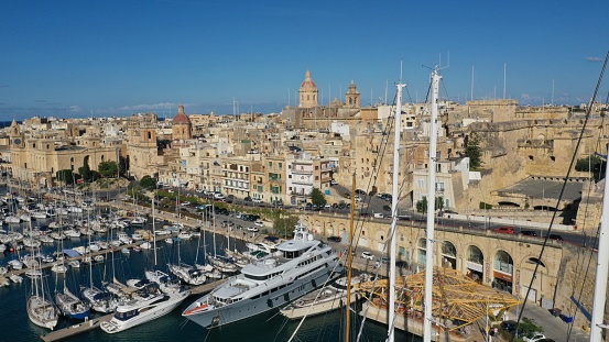 Aerial view of sailboats moored in harbour Senglea and Birgu, Bormla / Cospicua, Valletta, Malta. Ancient architecture of old town: christian orthodox churches, cathedrals, basilicas. Sunny day, blue sky. Summer travel destinations.