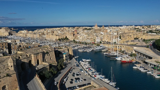 Aerial view of sailboats moored in harbour Senglea and Birgu, Bormla / Cospicua, Valletta, Malta. Ancient architecture of old town: christian orthodox churches, cathedrals, basilicas. Sunny day, blue sky. Summer travel destinations.