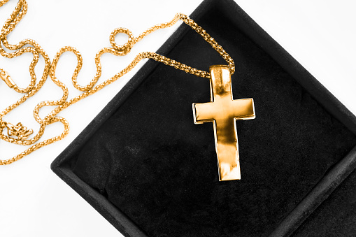 Large gold cross pendant on a chain in black jewel box closeup