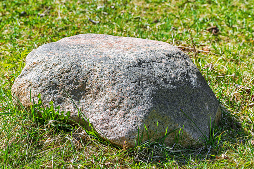 Large boulder with a flat top on a background of green grass. Focus on the foreground.