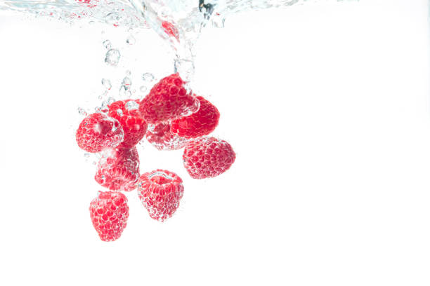 Raspberries splashing into crystal clear water with air bubbles