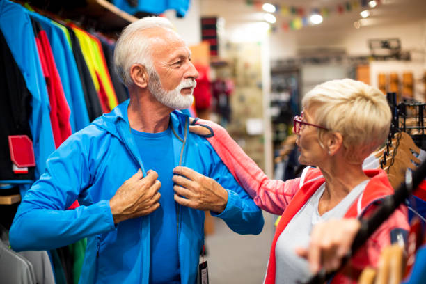 istock Senior male putting on a soft shell hiking jacket while his partner is standing by in a mountaineering equipment store 1226176759