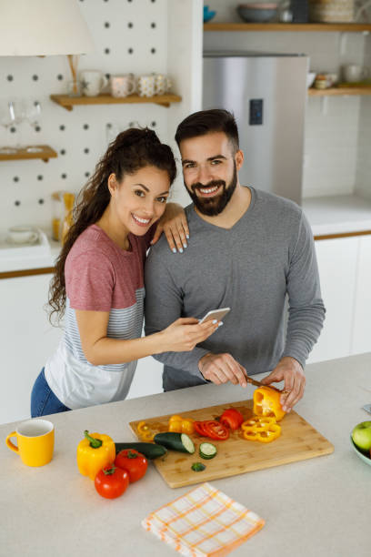 istock Young woman using her smart phone while her boyfriend prepares a meal 1226177602