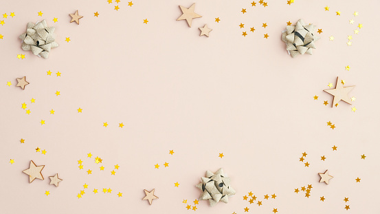 Frame of golden confetti and wooden stars on beige background. Flat lay composition for Birthday, Mother day or wedding.