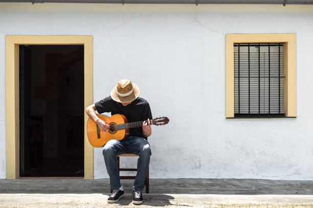 young man with straw hat playing classical guitar in front of the facade of his white house in the countryside on a sunny day. rural lifestyle. - musica sertaneja imagens e fotografias de stock