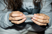 Young woman in tracksuit rolling a marijuana joint in the street at night. Details of hands rolling cannabis cigarette.