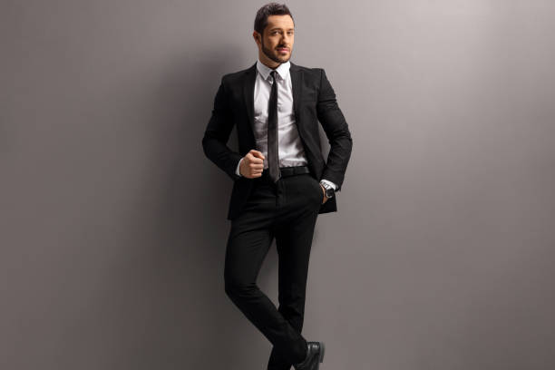 istock Male model in a black suit and tie leaning on a gray wall 1226181912