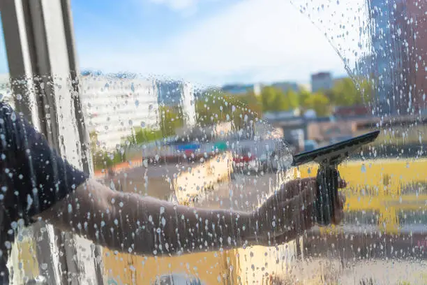 Photo of Rubber squeegee in male hand cleans a soaped window