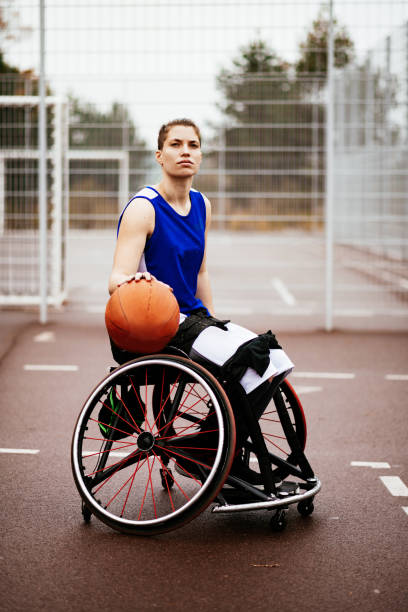 Generation Z woman in wheelchair playing basketball - preparation of sport wheelchair near the basketball court Disabled 20 y.o. woman in wheelchair, shooting basketball ball on the outdoor court on rainy day athlete with disabilities photos stock pictures, royalty-free photos & images