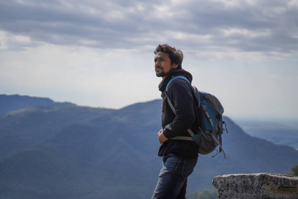 istock Young handsome indian boy standing on the top of the mountain with a bag pack while looking upwards in motivation 1226189825