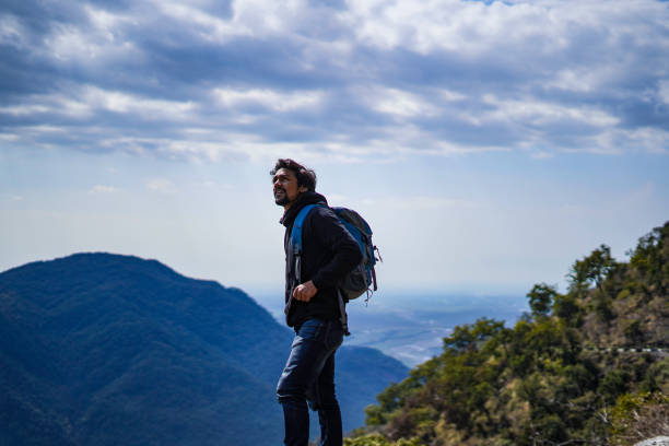 istock Young handsome indian boy standing on the top of the mountain with a bag pack while looking upwards in motivation 1226189829