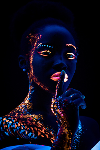 african woman with body art glowing in ultraviolet light. Portrait of beautiful woman painted in fluorescent powder. isolated dark space