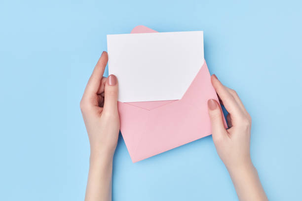 istock Pink envelope with blank white postcard in woman's hands on the blue background. Mail concept 1226192111