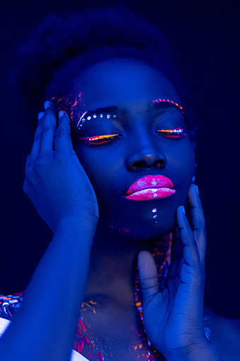 sensual young african woman with fluorescnet luminescence prints on skin, glowing in UV light. isolated space. fluorescent make-up, body art