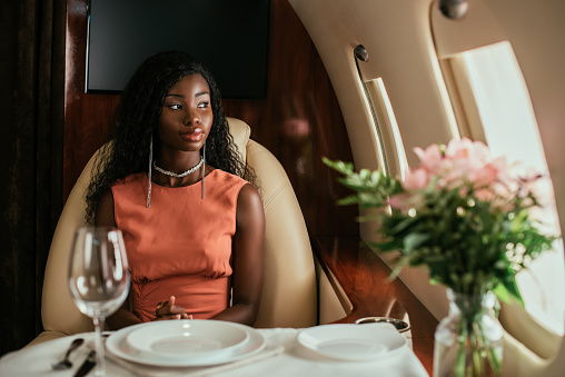 selective focus of dreamy african american woman sitting at served table in private plane