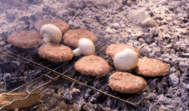 Beef BBQ Cooking of burger meat and mushroom. Iron barbeque grill pan with fire and food. Hamburgers outdoors barbecuing on coals. Closeup beef for burgers on cast iron grill. Juicy fat food grilled. barbacoa de ternera cocina de carne de hamburguesa y champiñones. barra de barbacoa de hierro con fuego y comida. hamburguesas al aire libre barbacoa en carbón. carne de primer plano para hamburguesas en parrilla de hierro fundido. jugosas grasas a la pa
