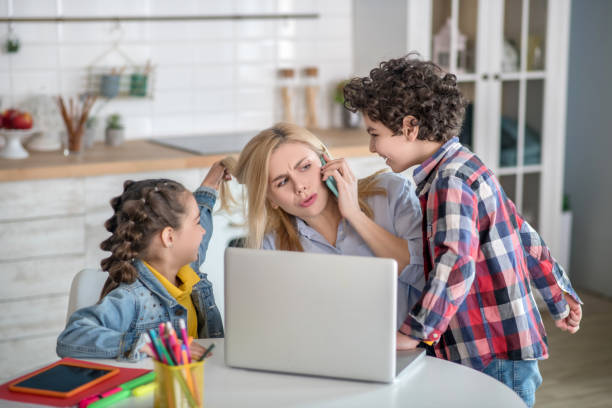 istock Blonde female working on laptop and talking on mobile, distracted by curly boy looking for her attention 1226199675