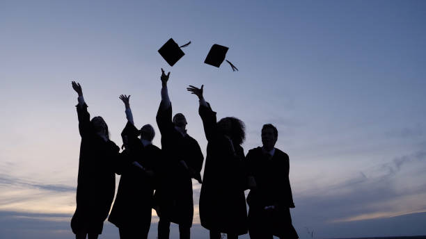 silhouette of graduating students throwing caps in the air - graduation imagens e fotografias de stock