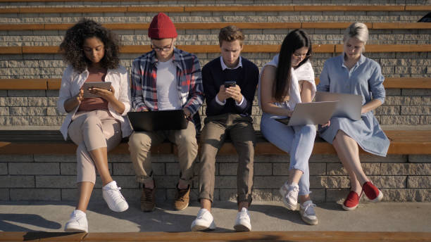 istock Multi-ethnic students sitting in a row absorbed by phones, compu 1226201759