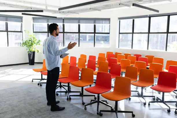 Side view of a Caucasian businessman wearing smart clothes, standing in an empty modern meeting room, training himself before a conference